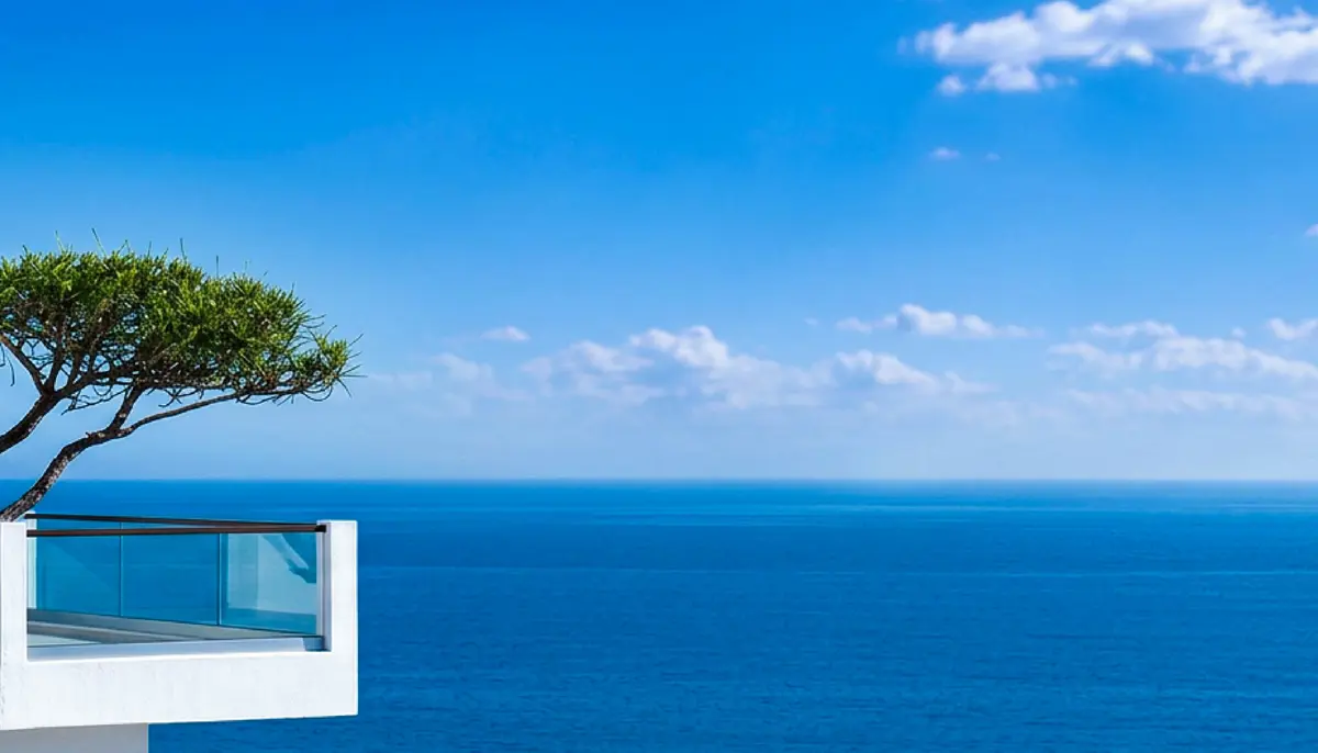 A glass balcony and pine looking out over deep blue sea to the horizon